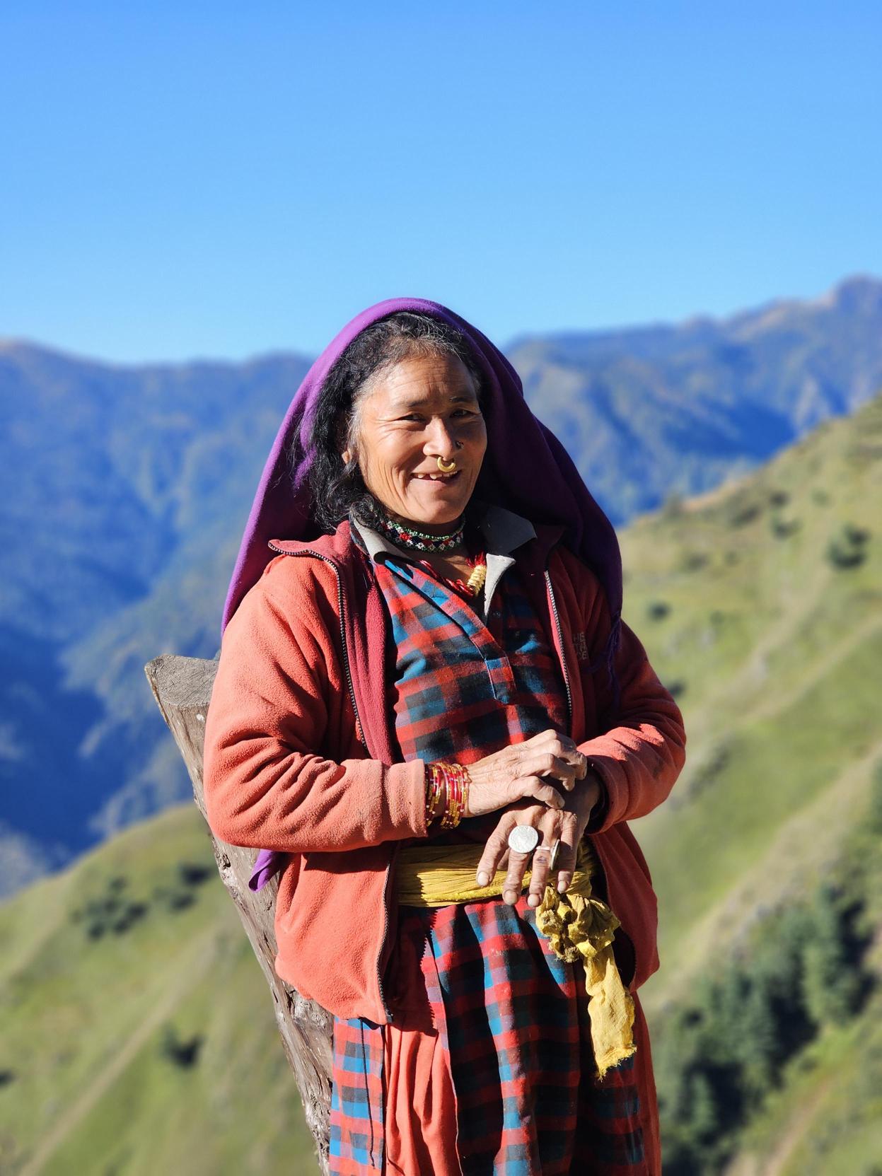 A smiling village woman in traditional dress against Himalayan backdrop